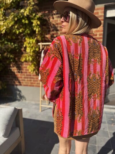 Femme blonde de dos veste lignée rose et rouge avec tigres